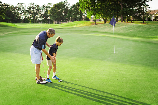 Father teaching daughter how to play golf.