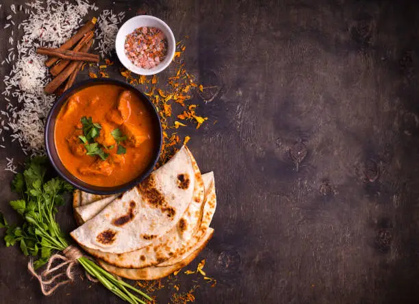 Spicy chicken tikka masala in bowl on rustic wooden background. With rice, indian naan butter bread, spices, herbs. Space for text. Traditional Indian/British dish. Top view. Indian food. Copy space