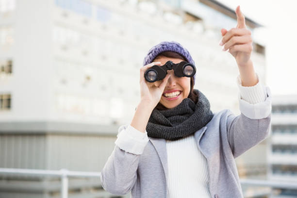 Smiling woman with binoculars pointing up outdoor