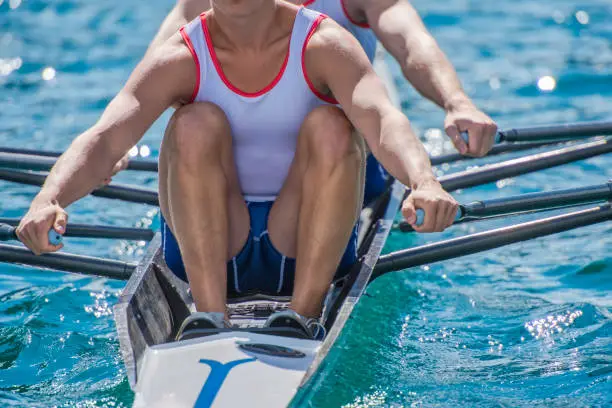 Front close up view of a two unrecognizable men in a sport rowboat on a lake race.
