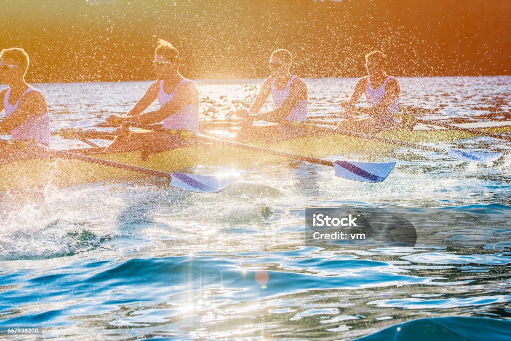 Four men rowing on a lake Side view of a coxless four training on a lake, copy space. Sport Rowing Stock Photo