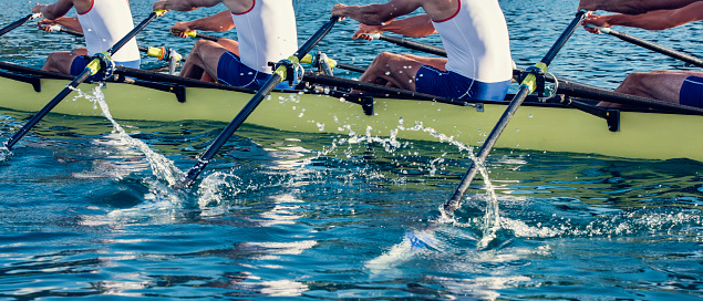 Side view of a four unrecognisable men rowing on wather, copy space.