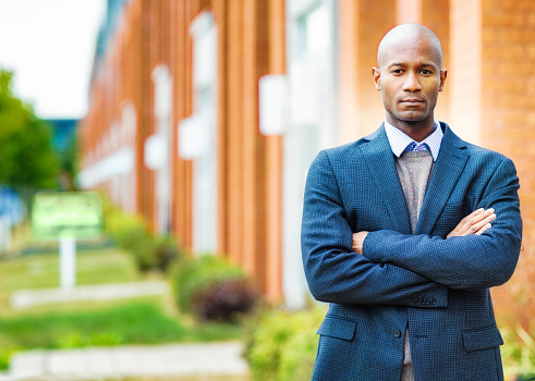 Single black man in suit serious Autumn portrait arms crossed with real estate background