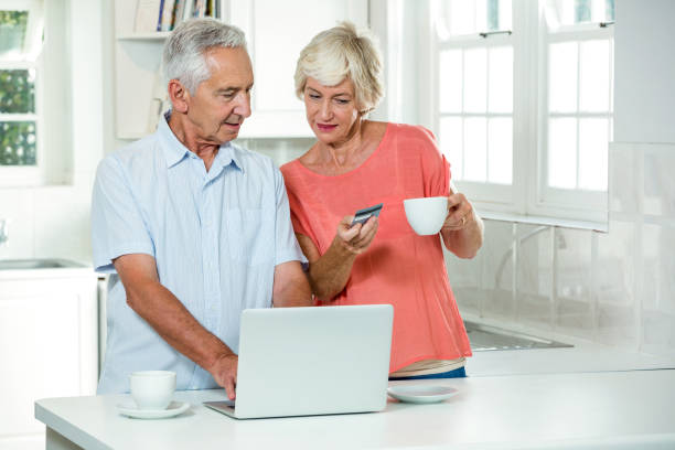 senior couple with credit card while using laptop - front view cup saucer white imagens e fotografias de stock