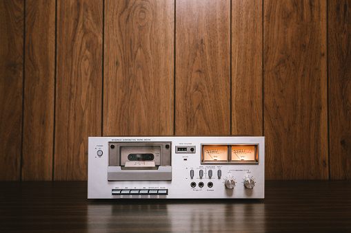 A vintage looking tape player / recorder stereo sits on the counter of a 1970's - 1980's  living room with wood paneling.   Horizontal image with copy space.