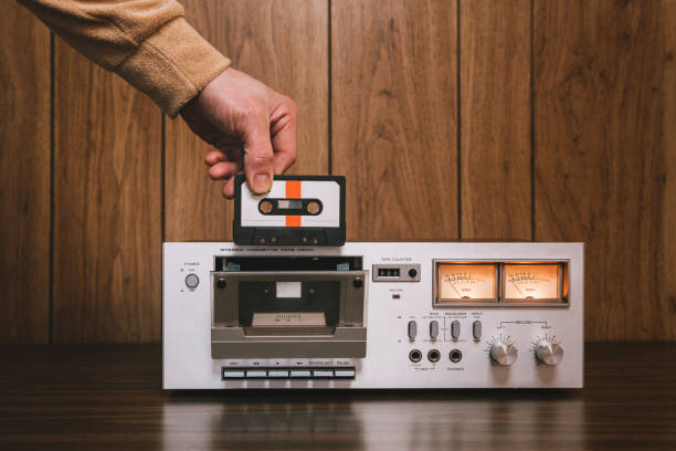 Cassette Player Stereo in Retro Style A vintage looking tape player / recorder stereo sits on the counter of a 1970's - 1980's  living room with wood paneling.  A mans hand reaches down to insert a cassette into the machine.  Horizontal image with copy space. audio cassette photos stock pictures, royalty-free photos & images