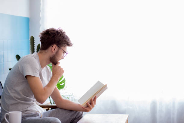 istock Young man reading book on sofa in the living room. 667979400