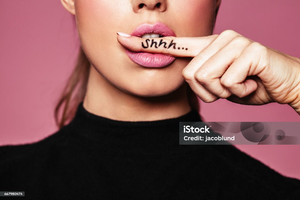 Shh! Women's secrets Shh! Women's secrets. Cropped shot of female with finger in mouth. Closeup portrait of young woman is showing a sign of silence with shhh written on the finger. Women Stock Photo
