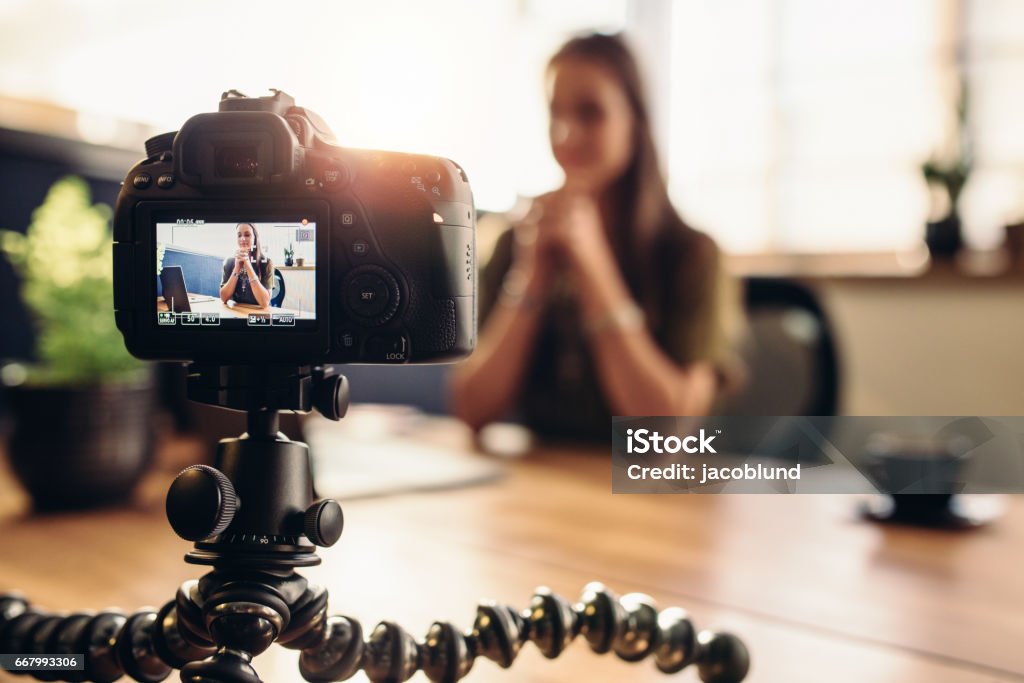 Fotocamera digitale su treppiede flessibile che registra un video di donna alla scrivania. - Foto stock royalty-free di Videocamera