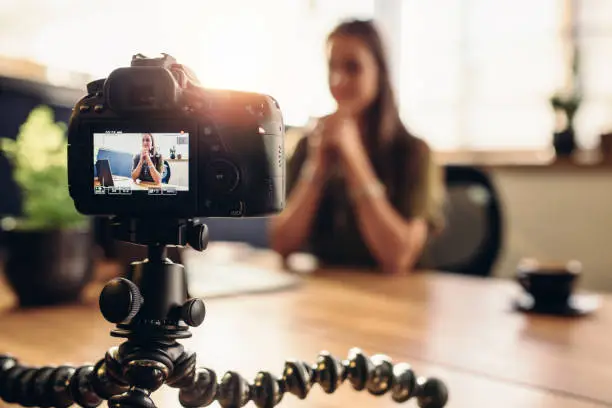 Female vlogger recording content for her video blog. Young woman in focus on digital camera screen.