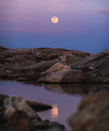 The Full Moon rises over a coastal landscape.