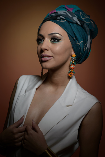 Beautiful woman in a turban.Young beautiful woman with turban and golden accessories.Beauty fashionable woman with hairs wrapped in turban. Pretty Caucasian model wearing  earrings  posing in studio.