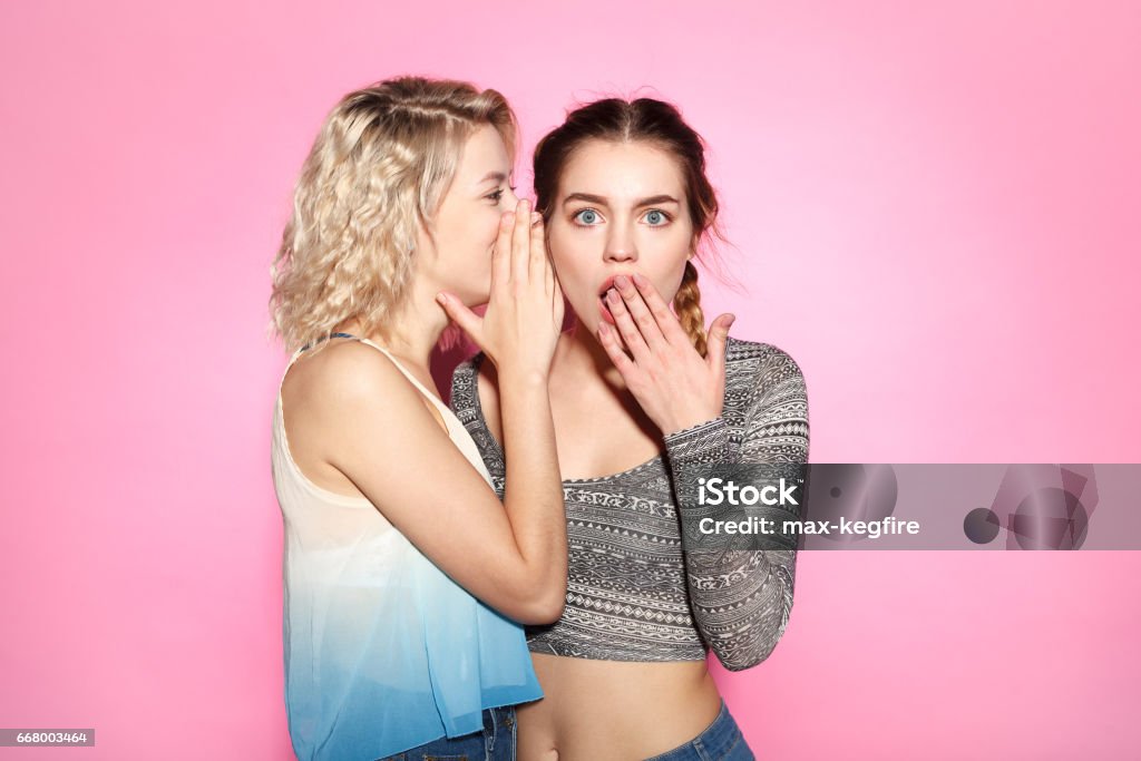 Two gossiping women Woman whispering to her friend's ear on the pink background. Whispering Stock Photo