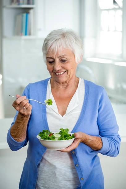 istock Senior woman eating salad while standing in kitchen 668027138