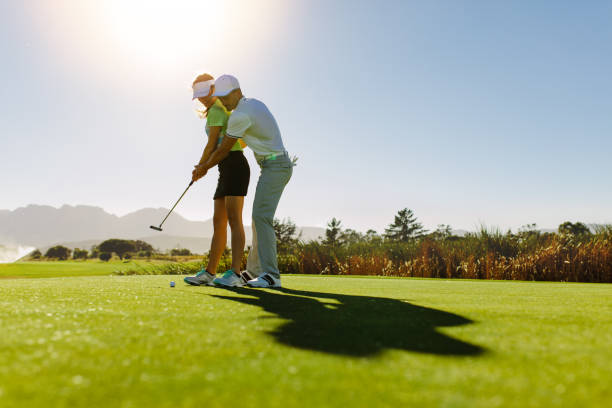 мужчина учит женщину играть в гольф на поле - putting together стоковые фото и изображения