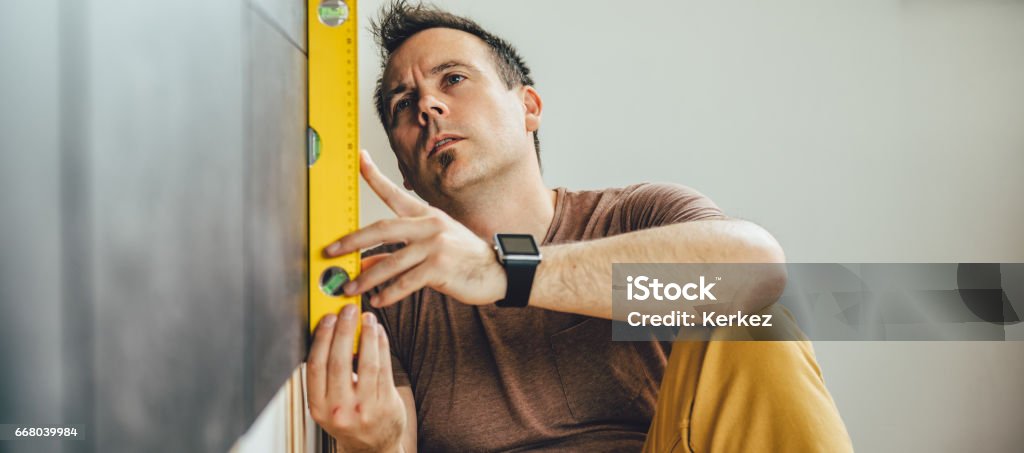 Man using leveling tool Man wearing brown shirt using leveling tool at home Level - Measurement Tool Stock Photo