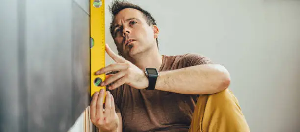 Man wearing brown shirt using leveling tool at home