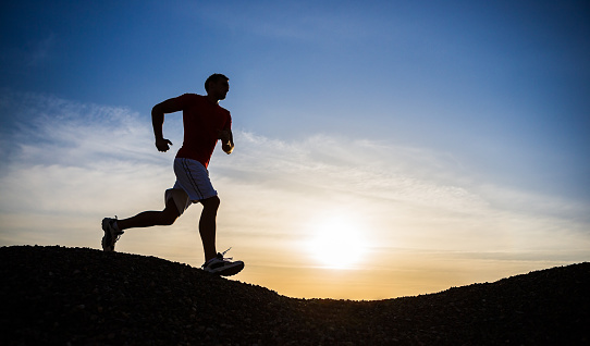 Male running down the mountain with setting sun behind.