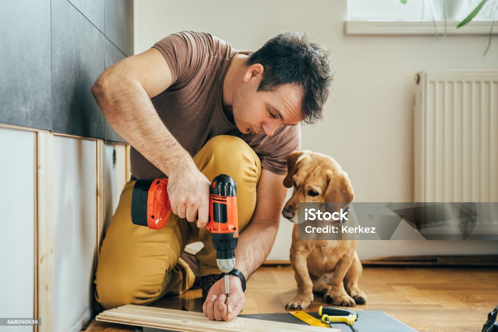Man and his dog doing renovation work at home Man doing renovation work at home together with his small yellow dog DIY Stock Photo