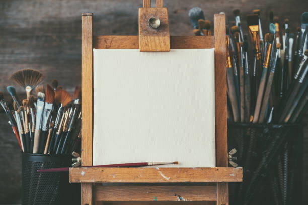 Artistic equipment in a artist studio: empty artist canvas on wooden easel and paint brushes Retro toned photo. stock photo