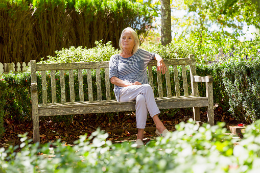 Portrait of modern, attractive mature woman sitting in the park in sunshine, full frame horizontal composition with copy space