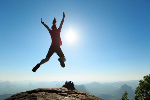 istock cheering successful young woman hiker jumping on mountain peak 668080286