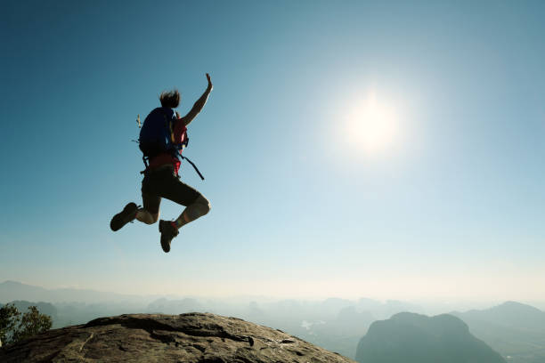 istock cheering successful young woman hiker jumping on mountain peak 668080716