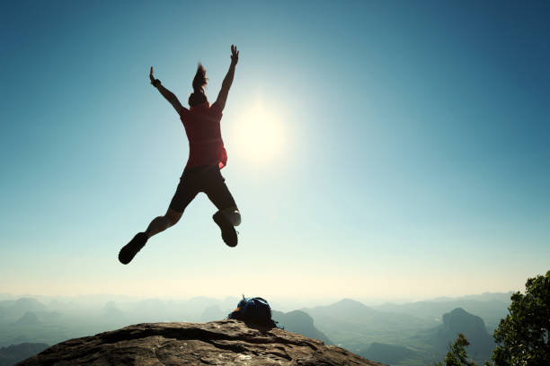 istock cheering successful young woman hiker jumping on mountain peak 668080880