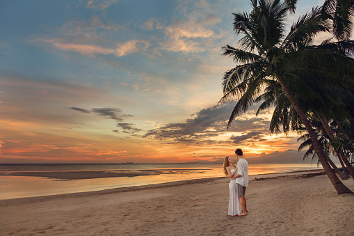 Young couple enjoy his honeymoon at the beach on tropical island. Sunset time