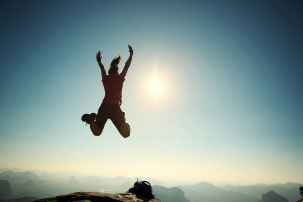 istock cheering successful young woman hiker jumping on mountain peak 668084252