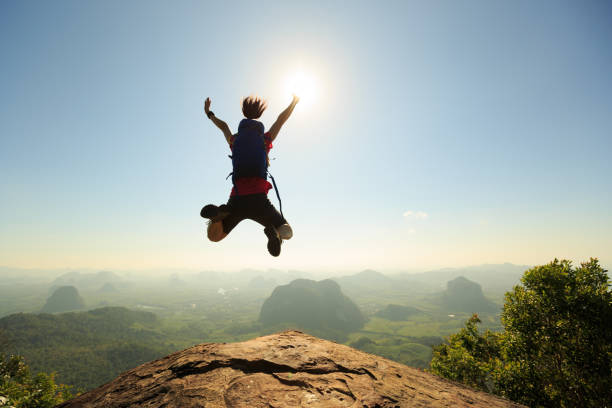 istock cheering successful young woman hiker jumping on mountain peak 668086486