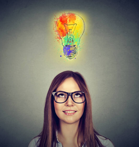 istock woman with glasses and colorful idea looking up at light bulb 668087100