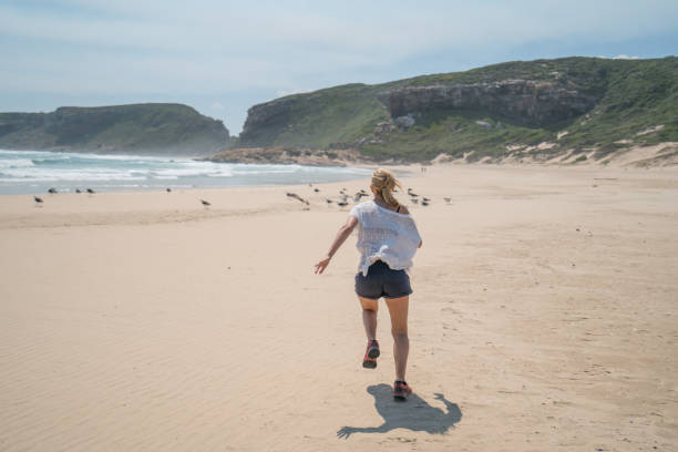 istock Young woman running to birds on beach 668110728