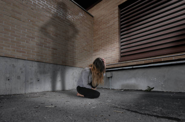 Beautiful young brunette woman in a sweater and jeans is upset and sits near a wall in a tunnel, back light and toning, copy space