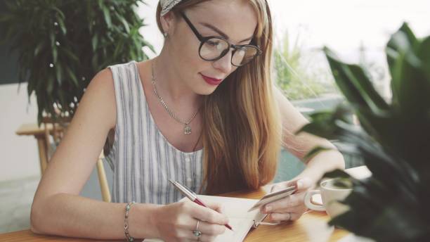 istock Young pretty woman writing information from card to notebook . 668129482