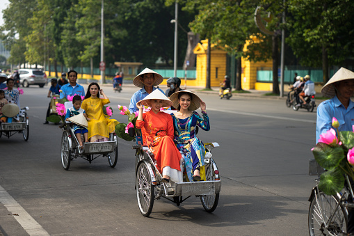 Hanoi, Vietnam - Oct 16, 2016: Vietnamese girl wears traditional long dress Ao Dai going by Cyclo (pedicab) on Hanoi street