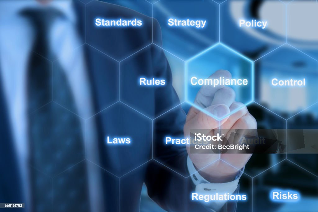 Hexagon grid compliance click from businessman Businessman in blue suit in front of office background clicking tile with the word compliance in hexagon grid Conformity Stock Photo