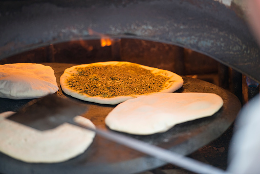 Baker putting pita bread with Za'atar spice into tabun oven.