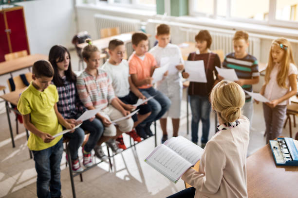 Above view of teacher rehearsing with choir of children. High angle view of music teacher singing with group of children in the classroom. school choir stock pictures, royalty-free photos & images