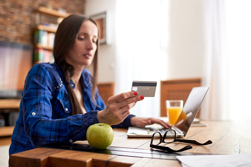 Woman is holding credit card and using laptop computer in order to buy products online.