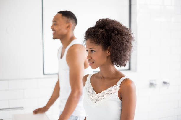 Couple in front of bathroom mirror Young couple standing in bathroom at home looking in mirror stock pictures, royalty-free photos & images