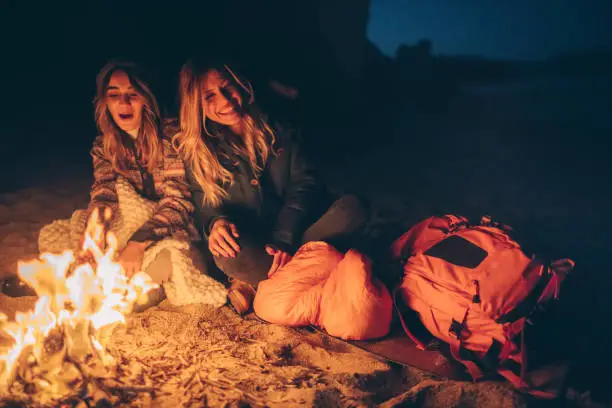 Photo of a couple of friends spending cool evening on the beach, sitting by the campfire