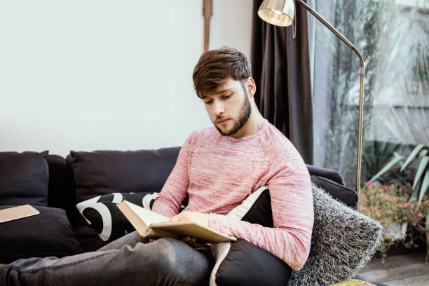 istock Attractive young man reading book on the couch 668190396