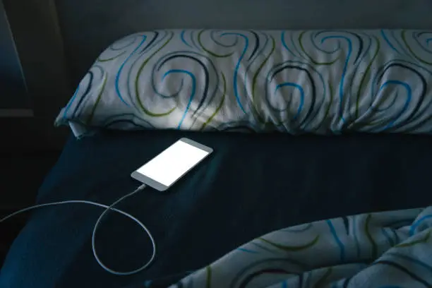 A smartphone in bed at night, with its screen illuminated.
