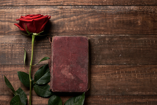 a red rose and an old book on a rustic wooden table, with a blank space, for Sant Jordi, the Catalan name for Saint Georges Day, when it is tradition to give red roses and books in Catalonia, Spain