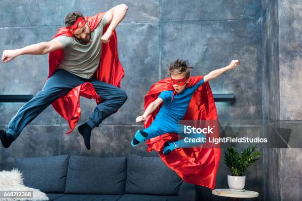 父と息子の自宅のソファの上にジャンプのスーパー ヒーロー衣装 - スーパーヒーローのストックフォトや画像を多数ご用意 - スーパーヒーロー, 父親, 子供