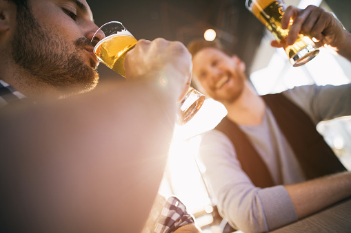 Low angle view of young man drinking beer while enjoying in a bar with a friend.