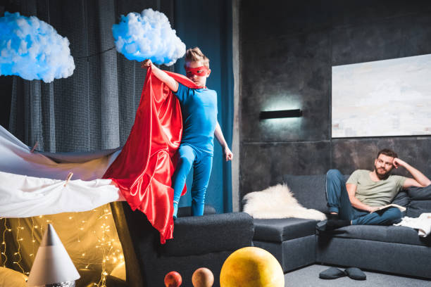 istock son in red superhero costume playing at home, father sitting on sofa behind 668214828