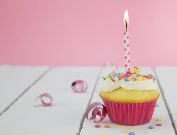 istock One cupcake with lit candle on white table against pink background - selective focus 668218858