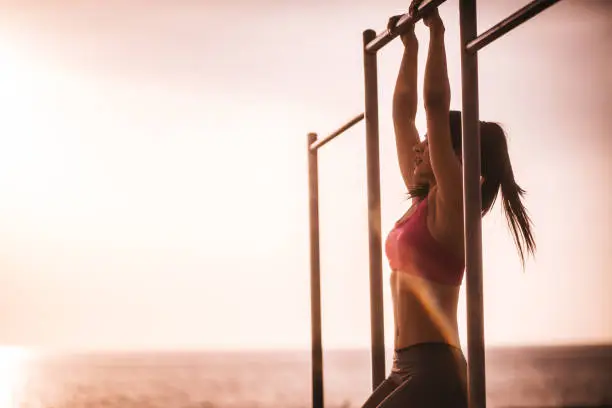 Young female fitness model doing pull ups at sunset next to the beach